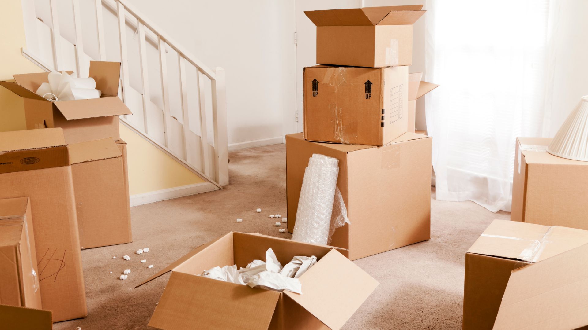 Moving day with cardboard boxes scattered near stairs in empty room