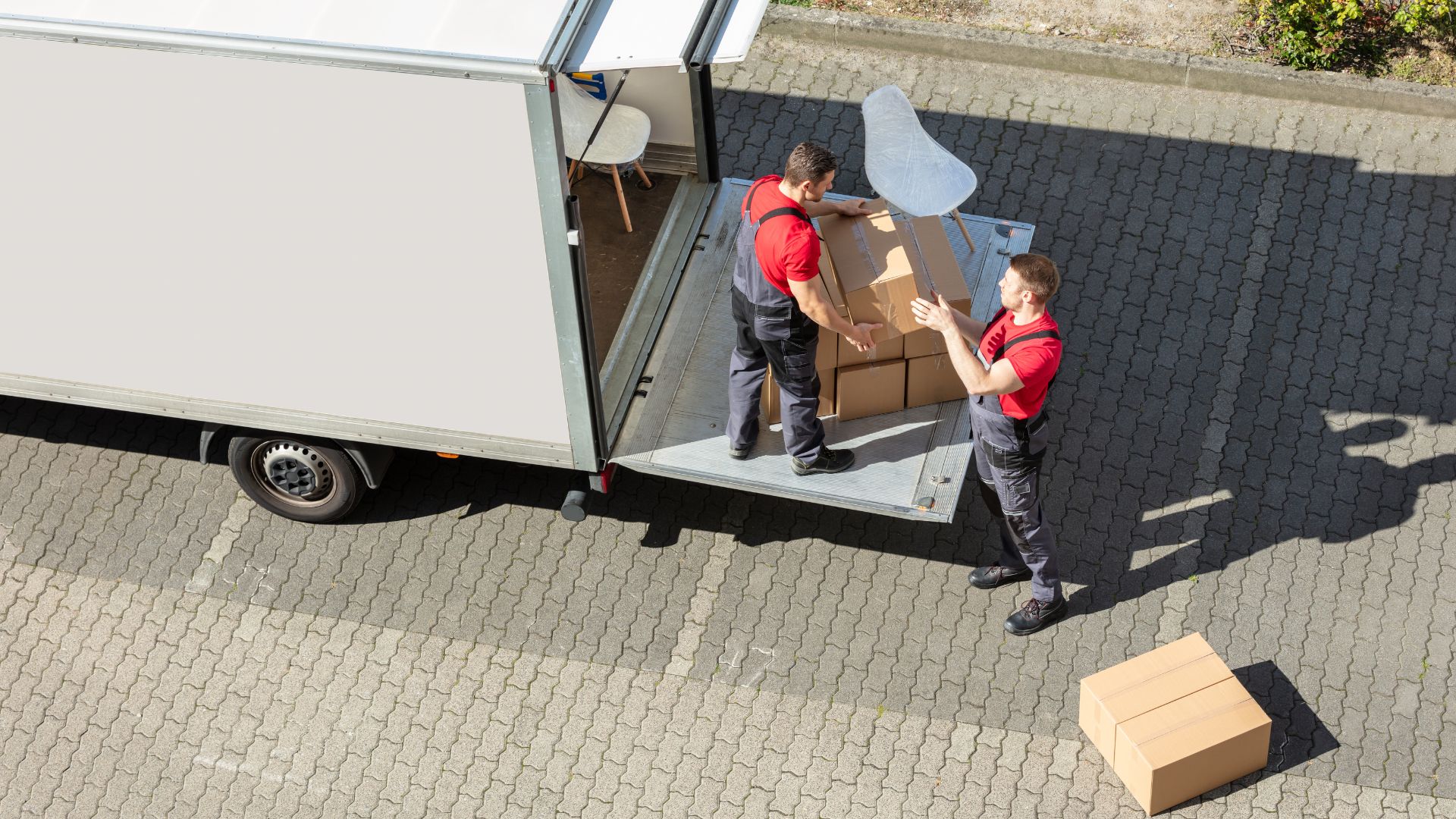 Two movers loading cardboard boxes into a delivery truck from a loading dock