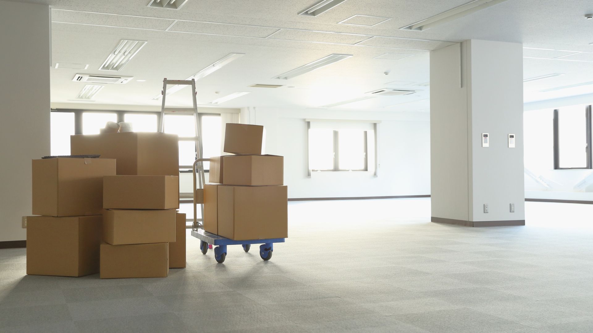 Moving boxes stacked on floor with hand truck in empty office space