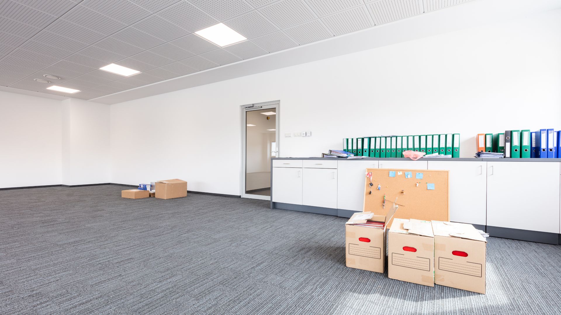 Empty office with cardboard boxes, file cabinets, and gray carpet