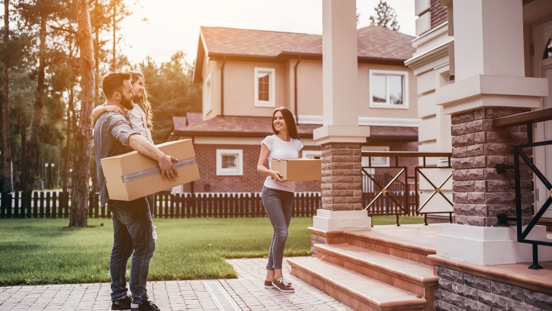 Couple carrying moving boxes in front of new home at sunset