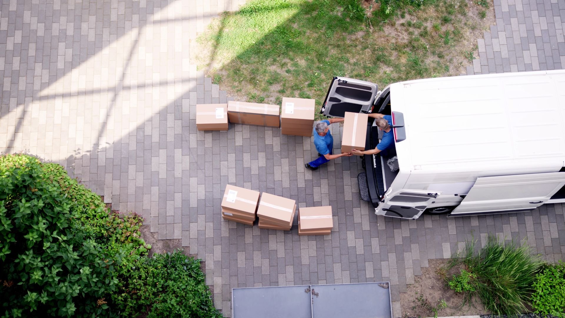 Delivery workers unloading cardboard boxes from white van on brick pavement