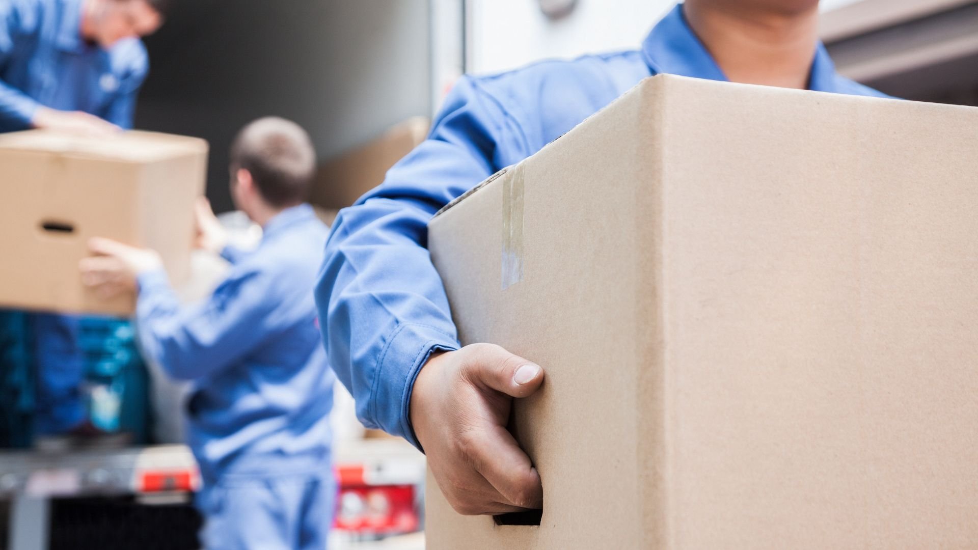 Movers in blue uniforms carrying cardboard boxes during relocation